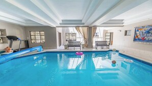 An indoor swimming pool with a blue tiled floor, a treadmill, and a bench. - Family Suite - Indoor Hot Tub, Heated Pool, Play Park & Table Mountain Views (Cape Town)