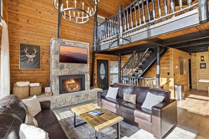 Ein rustikales Blockhaus-Interieur mit Kamin aus Stein, Ledersofas, einer Holztreppe und einer Kristallleuchter.