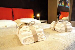 Ein ordentlich bezogenes Bett mit weißen Leinentüchern und einem beigen Band, eine Nachttischlampe und ein rotes Kopfteil.