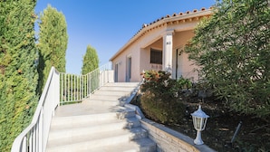 Une maison avec un escalier menant à la porte d’entrée, entourée de verdure et d’un lampadaire.