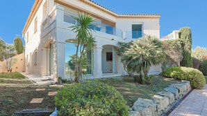 Une maison moderne à deux étages, avec une façade blanche, de grandes fenêtres et un chemin en pierre menant à l’entrée.
