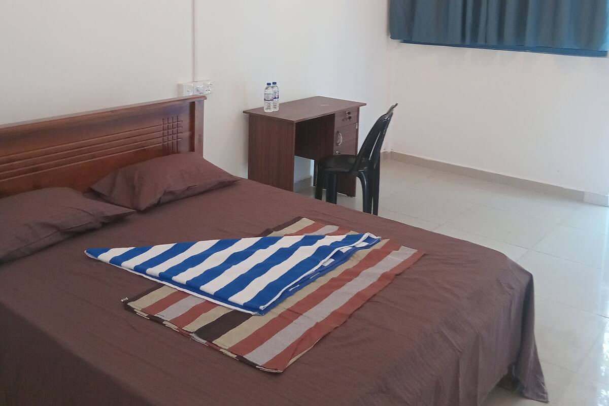 A bedroom with a bed, a desk, a chair, a ceiling fan, and a window with curtains.