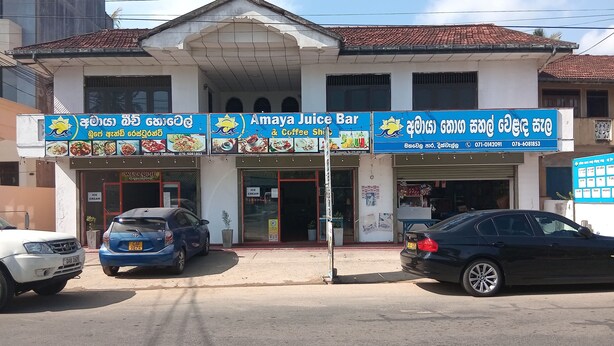 A two-story building with a sign for 'Amaya Juice Bar' and 'Coffee Shop'. There are two cars parked in front. -  Amaya Hotel and Restaurant (Dikwella)