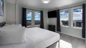Ett modernt hotellrum med en stor säng, två fönster med gardiner, en platt-TV och utsikt över staden.