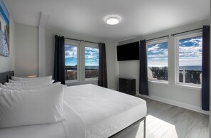 A modern hotel room with a large bed, two windows with curtains, a flat-screen TV, and a city view. - Monthly Rental in Brand New Boardwalk Condo + 100 Dollar Resort credit (Myrtle Beach)