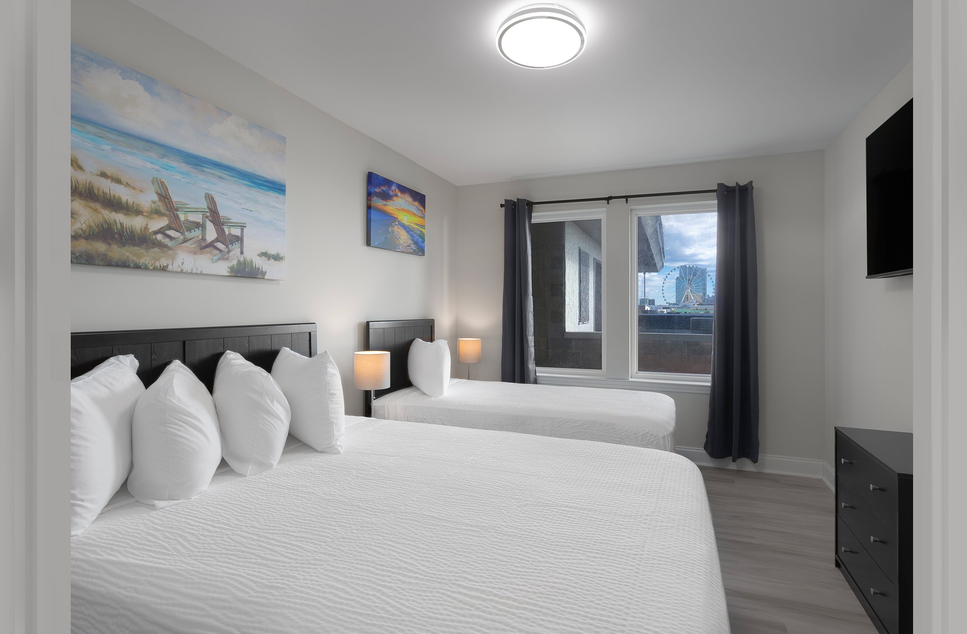 A hotel room with two beds, a large window with curtains, a flat-screen TV, and artwork on the walls.