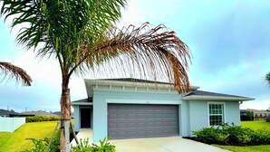 Una casa moderna de dos pisos con garaje, rodeada por un césped bien cuidado y una palmera.