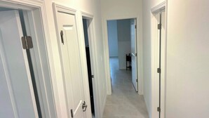 Un pasillo con puertas blancas y suelo de baldosas que conduce a una habitación con una silla negra.