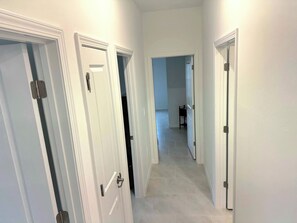 A hallway with white doors and a tiled floor, leading to a room with a black chair. - Spacious, brand-new and modern 4-bedroom house in Paradise (Rotonda West)