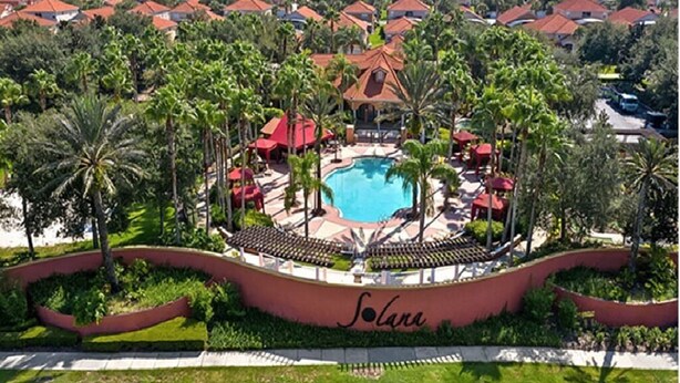 Een resort met een centraal gelegen zwembad, omgeven door palmbomen en gebouwen met rode daken.