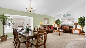 Een ruime woonkamer met een eethoek, met een kroonluchter, een zithoek en potplanten.