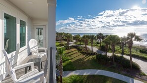 A balcony with white chairs and a view of a landscaped area with palm trees and a pathway leading to the beach. - Stay In Our Winter Rental On MB Boardwalk + 100 Dollar Resort credit (Myrtle Beach)
