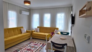 Ein Wohnzimmer mit zwei gelben Sofas, einem gemusterten Teppich, einem karierten Tisch und einem Fernseher an der Wand.