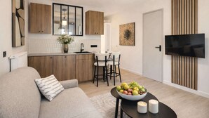 Eine moderne Küche mit Holzausstattung, ein Essbereich mit Tisch und Stühlen, ein Sofa mit Kissen sowie ein an der Wand befestigter Flachbildfernseher.