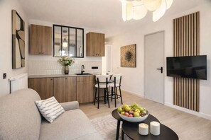 A modern kitchen with wooden cabinets, a dining area with a table and chairs, a sofa with a cushion, and a flat-screen TV mounted on the wall. - Ideal Parisian apartment close to Montparnasse (Paris)
