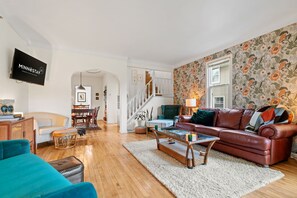 A living room with a brown leather sofa, a teal armchair, and a wooden coffee table. A flat-screen TV is mounted on the wall. - D. Musee Northeast (Minneapolis)