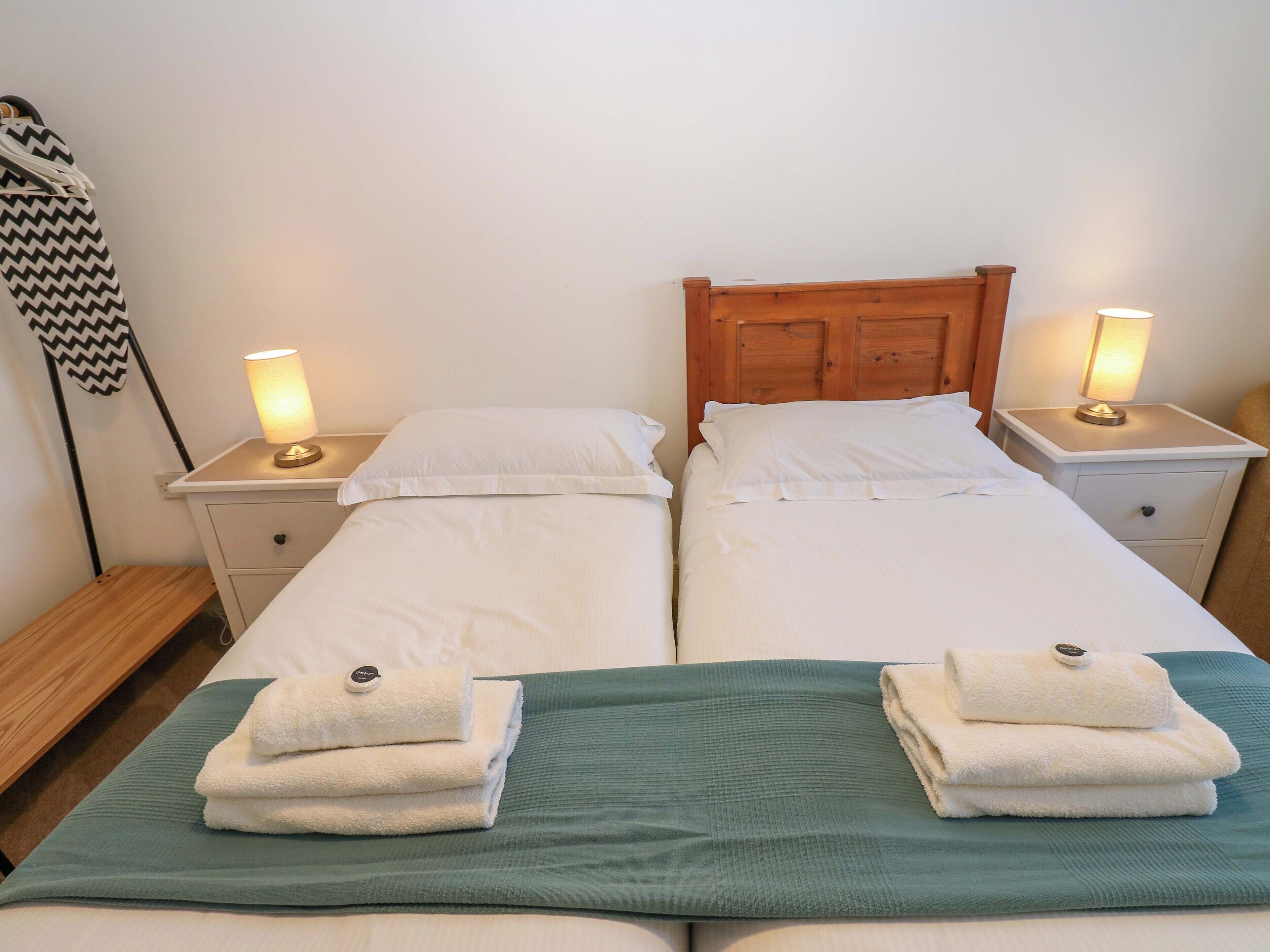 Uma cama de casal com lençóis brancos, duas mesas de cabeceira com luminárias e um cobertor verde.