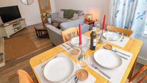 Ein Essbereich mit einem Holztisch, gedeckt für vier Personen, umgeben von Stühlen. Im Hintergrund befindet sich ein Fernseher und eine Couch.