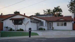 A two-story house with a red-tiled roof, a garage, and a small front yard with a lawn and a mailbox. - Terrific 3-bedroom house with AC in sunny Oceanside (Oceanside)