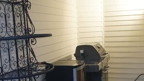A patio with a grill, a metal table with a chair, and a metal shelf unit. - Terrific 3-bedroom house with AC in sunny Oceanside (Oceanside)
