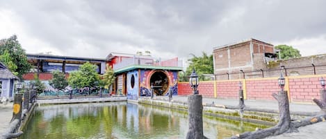 A courtyard with a pond, a building with colorful murals, and a brick wall.