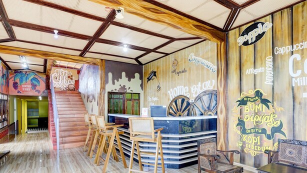 Interior de una cafetería con techo de madera, una barra con un letrero que dice "Cappuccino" y un mural en la pared.