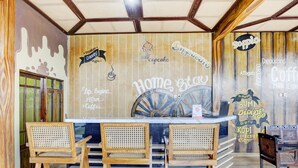 Un café con interior de madera, una barra con tres taburetes y decoración en las paredes, incluyendo un letrero que dice "Home & Coffee".