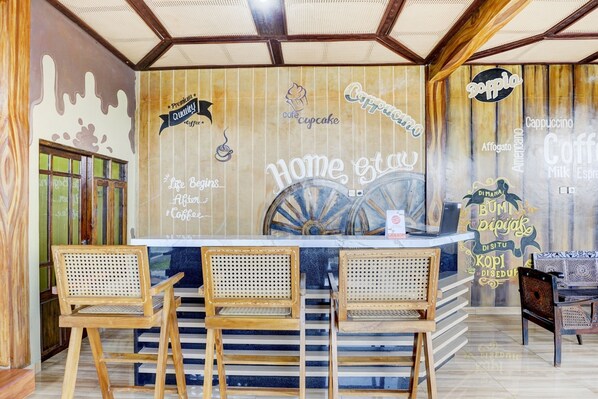 A café with a wooden interior, a counter with three stools, and wall decorations including a sign that says "Home & Coffee." - OYO 90303 Cafe & Homestay Kolam Pancing (Malang)