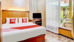 Habitación de hotel con una cama grande, televisión, cabecera de madera y vistas al balcón exterior.