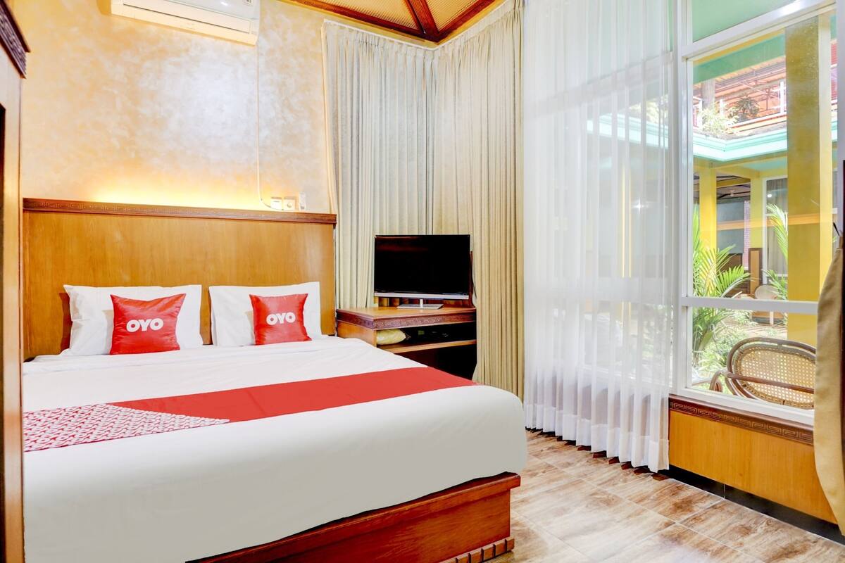 Habitación de hotel con una cama grande, televisión, cabecera de madera y vistas al balcón exterior.
