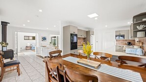 A modern kitchen with a dining area, featuring a wooden table, chairs, and a central island. - Bay Bliss - Fireplace - 3 Mins Walk to Beach (Callala Beach)