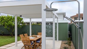 A covered patio area with a table and chairs, and a shower with a curved design. - Bay Bliss - Fireplace - 3 Mins Walk to Beach (Callala Beach)