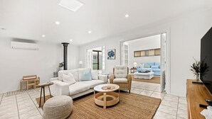 A modern living room with a white sofa, a round wooden coffee table, and a blue sofa in the background. - Bay Bliss - Fireplace - 3 Mins Walk to Beach (Callala Beach)