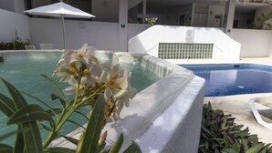 Ein Poolbereich mit Whirlpool, umgeben von weißen Wänden und einem Reetdach.
