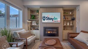 Un salon moderne doté d’une cheminée, de sièges confortables et d’un grand écran de télévision diffusant une publicité pour « StayIn ».