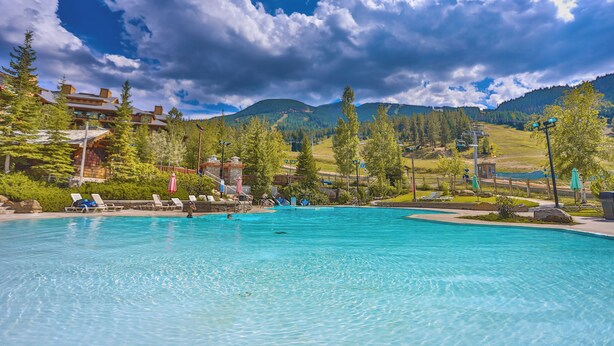 Une piscine entourée d’arbres et de montagnes, avec des chaises longues et des parasols.