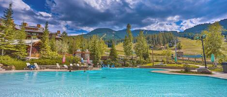 A swimming pool with lounge chairs and umbrellas, surrounded by trees and mountains.
