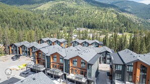 Un hôtel moderne composé de plusieurs bâtiments, chacun doté de grandes fenêtres et d’un toit en pente, et qui se distingue sur un arrière-plan de forêt dense et de montagnes.
