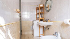 Ett badrum med tvättmaskin, handfat, spegel och en hylla med toalettartiklar.