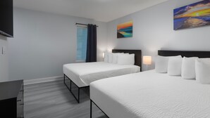 Een hotelkamer met twee bedden, een flatscreen-tv, een schilderij en een raam met gordijnen.