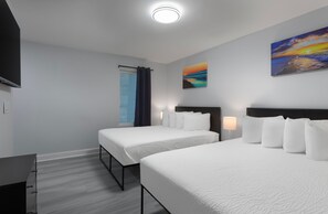 Une chambre d’hôtel avec deux lits, un téléviseur à écran plat, un tableau et une fenêtre avec des rideaux.