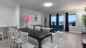 Een moderne eethoek met een donker houten tafel en witte stoelen, een blauwe bank en een groot raam met gordijnen.