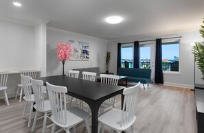 Un espace repas moderne avec une table en bois foncé et des chaises blanches, un canapé bleu et une grande fenêtre avec des rideaux.