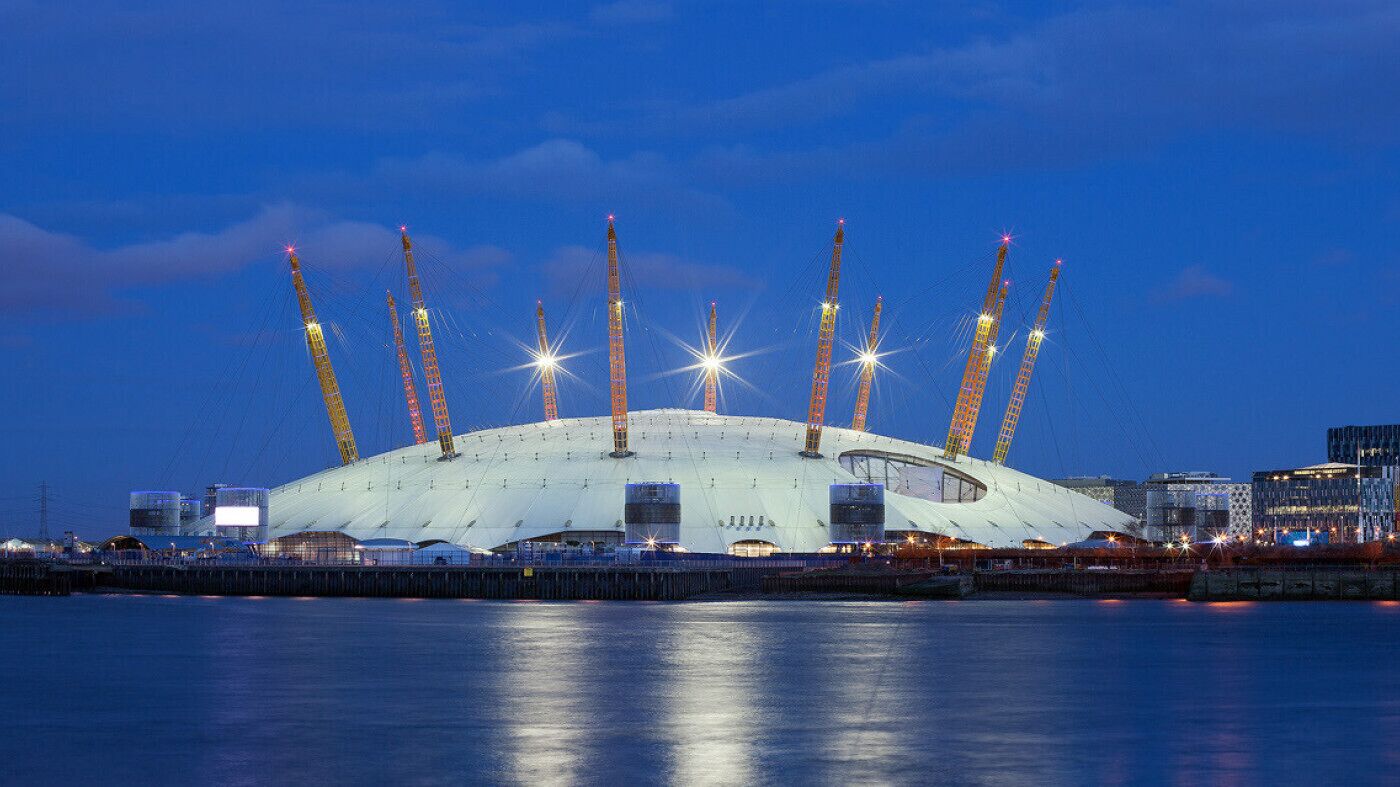 A large stadium with a unique roof structure and multiple cranes around it.