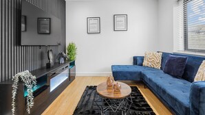A modern living room with a blue sofa, a round coffee table, and a flat-screen TV mounted on a wall. - Cozy  2-bedroom apartment in Canning Town near Excel London (London)