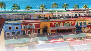 A coastal street with colorful buildings, palm trees, and a beach in the background.