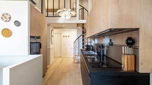 A modern kitchen with a black countertop, wooden cabinets, and a staircase leading to an upper level.