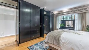 A bedroom with a bed, a large wardrobe, a window with curtains, and a plant. - Indoor Solar Heated Pool, Hot Tub, PlayPark, BBQ Room, Table Mountain Views WiFi (Cape Town)