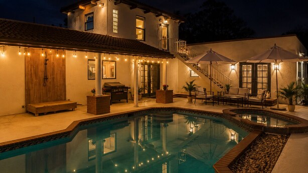 Ein Poolbereich mit einem Haus, Sitzgelegenheiten im Freien und Lichterketten.