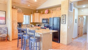 A kitchen with wooden cabinets, a central island with bar stools, a refrigerator, and a microwave. - Bela's in Torreon with Golf Membership (Show Low)